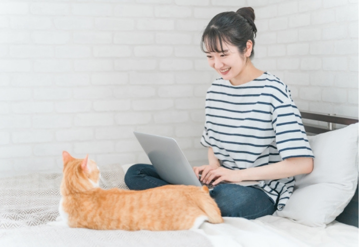 猫のいるベッドの上でパソコンを使う女性